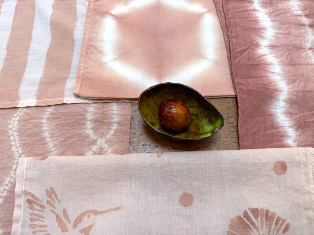 Photo of Sophy's avocado-dyed cottons and silks with an avocado skin and pit in the center.